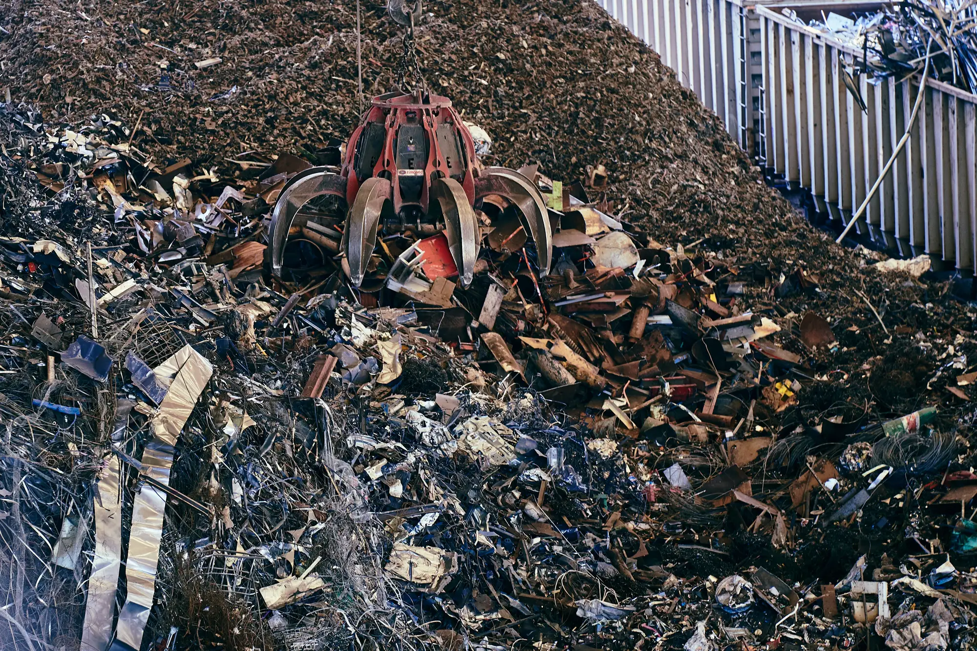 A red orange-peel grapple biting into a pile of shredded scrap steel